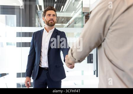 Professional welcome gesture between two individuals in a contemporary office environment, symbolizing agreement or collaboration. Stock Photo