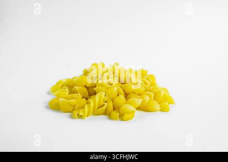 Close-up view of a small pile of uncooked conchiglie pasta on a plain white background. The pasta is bright yellow and has a shell-like shape. The foc Stock Photo