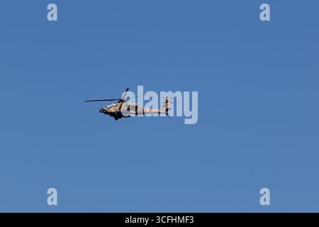 Israel Air Force AH-64 Apache attack helicopter in flight, stores fitted, desert tan scheme, rotor turning under clear blue sky, location unspecified. Stock Photo
