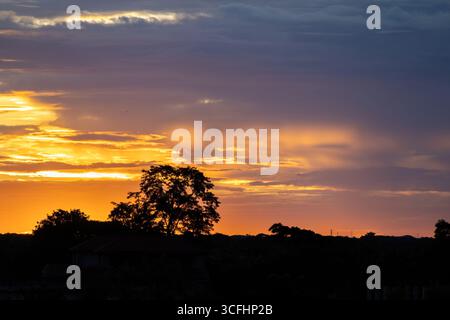 Beautiful morning sky at sunrise. A fiery red sunrise casts a dramatic glow over the silhouette of a forest. Stock Photo