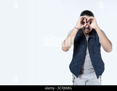 Man gesturing binoculars with his hands on isolated background. Latino man looking through his hands on white background Stock Photo