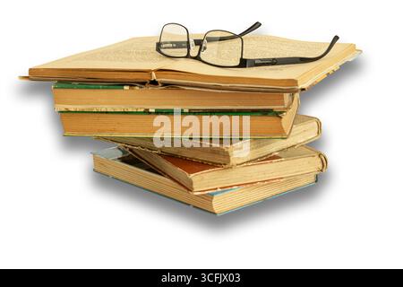 Old books stacked on top of each other, worn from reading. The top book is well lit with glasses on it, against a white background. Stock Photo