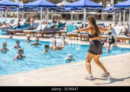 A young female Sports Animator is doing water aerobics for people in the pool of a hotel resort. Stock Photo