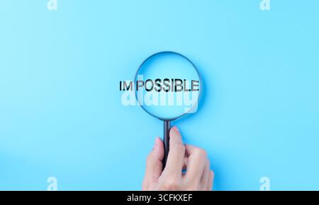Hand holding magnifying glass focuses on possible from the word impossible on a light blue background. possible motivational inspirational, Business m Stock Photo