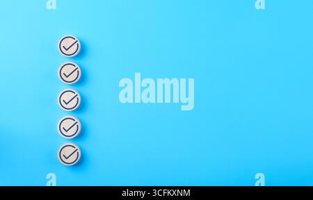 Checklist concept. Correct sign tick check mark on wooden block with copy space for the checklist on blue background. Business survey questionnaire, Stock Photo