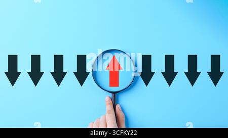 Difference concept. A single red upward arrow is view through magnifying glass among black downward arrow on blue background. Think different, find Stock Photo