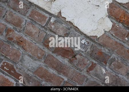 Tilted view of an exterior brick wall partially covered with cracked, crumbling white plaster. Taken in Centralia, Missouri, USA. Stock Photo