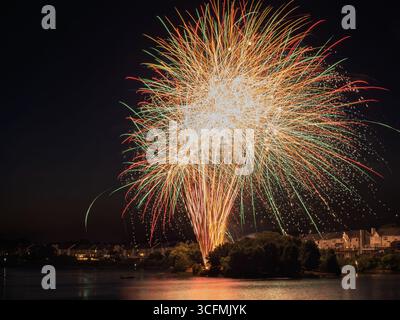 A colossal, dazzling burst of gold, green, and red fireworks illuminates the night sky over Lake Ashburn in Ashburn Village, Virginia. Stock Photo