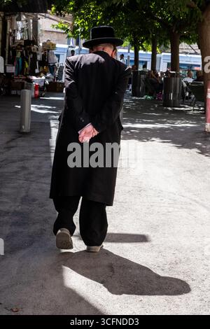 A religious, Jewish man walks on a Jerusalem sidewalk with his hands clasped behind his back. Stock Photo