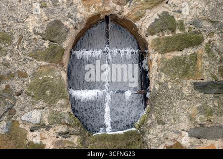Old window and bars covered with frost crystals in the stone wall of a historic church at village Stock Photo