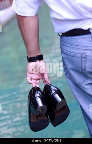 Back view, a young executive man in a white shirt and blue jeans with shoes in his hand. Stock Photo