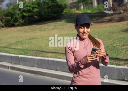 Young Latina woman smiling while using her phone outdoors Stock Photo
