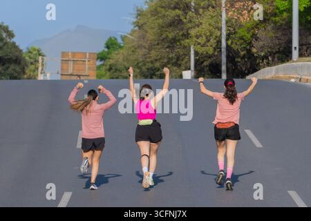 Three Latina women running and celebrating on a wide open road Stock Photo