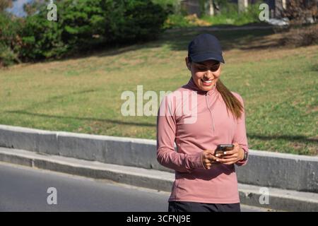 Young Latina woman checking her phone while walking outdoors Stock Photo