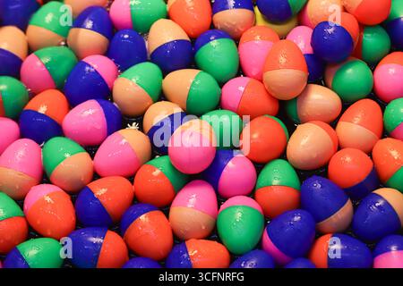 Glossy colorful plastic eggs in two-tone shades floating on water, vibrant abstract background with playful reflections and rainbow sparkles. Stock Photo