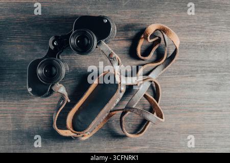 Old vintage binoculars on a wooden background, top view, close up. Obsolete military binoculars USSR times Stock Photo