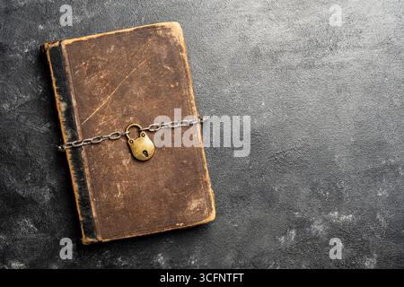 Metal chain and padlock around old book on black background, close up, top view. Copy space for text Stock Photo