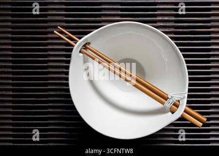 A pair of chopsticks lying across an empty white soup bowl on wooden striped tray, close up, top view Stock Photo