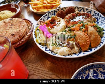 Lebanese food with hummus, tahini, falafel, tabbouleh, pita bread and savoury pastry puffs served on patterned ceramic plates with pickles Stock Photo