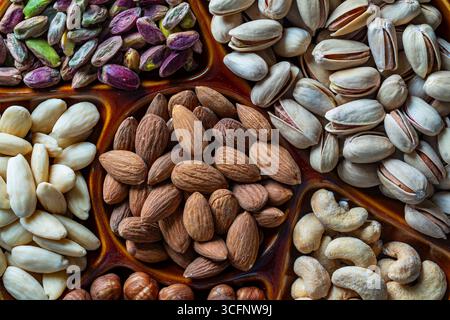 Assortment of nuts in ceramic bowl on a background, close up, top view, copy space. Cashew, hazelnuts, pistachios and almonds nuts for eat. Vegetarian Stock Photo
