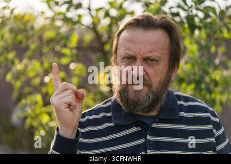 Portrait of a thinking or solve problems senior man. Elderly bearded caucasian male in nature. Face bearded upset male waving his finger, close up Stock Photo