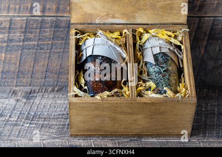 Glass jar with of flower tea and a glass jar with of pine cone jam in a wooden gift box on a table, close up. Beautiful present for family and friends Stock Photo