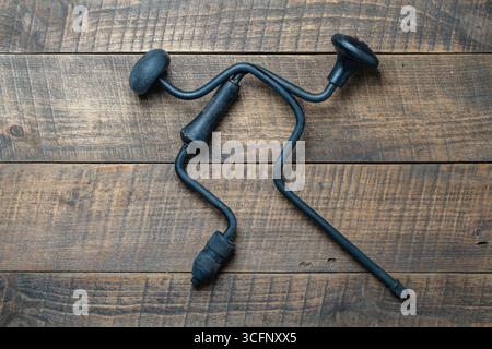 Two crossed black old hand drill on wooden background, top view, close up Stock Photo