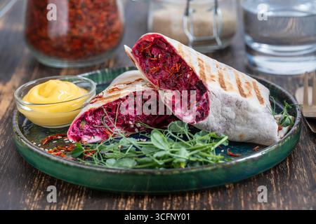 Vegan burrito. Sliced up raw food wrap with red beetroot, feta cheese, prunes, dill and cream sauce with pea microgreens on a plate. Close up Stock Photo