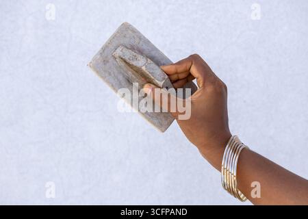 Female hand holding a well-worn wooden trowel. The tool is used for smoothing and leveling freshly laid plaster or concrete surfaces during constructi Stock Photo