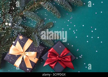 Gift boxes with red and golden bow and fir branches on dark green background with confetti. Top view, flat lay, copy space. Stock Photo