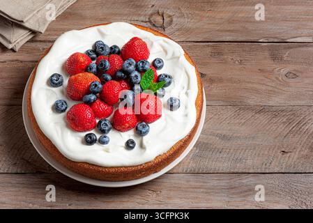 Sponge cake with cream cheese and fresh summer berries on wooden background,  copy space. Homemade Victoria cake with whipped cream, strawberries and Stock Photo