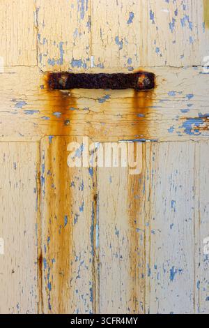 Rusty Metal Handle on Weathered Wooden Door with Peeling Yellow Paint Stock Photo