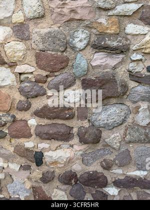 Closeup of an old stone wall with aged surface and mortar, featuring irregular blocks in brown, grey and beige tones typical of historic architecture Stock Photo