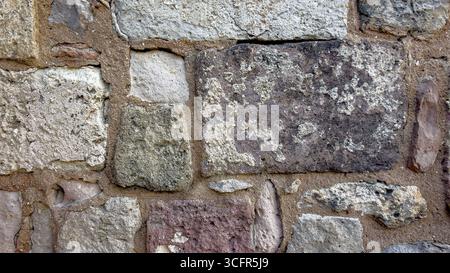 Closeup of an old stone wall with aged surface and mortar, featuring irregular blocks in brown, grey and beige tones typical of historic architecture Stock Photo
