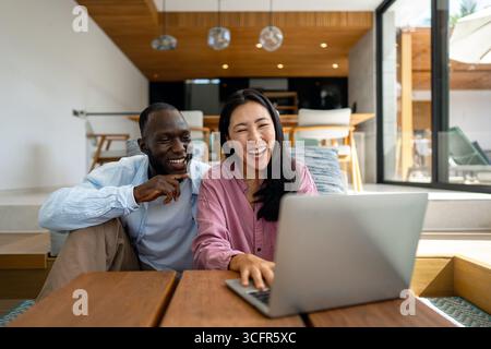 Young happy multiethnic couple having fun while using laptop at home. Happy couple discussing future Stock Photo