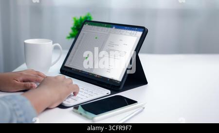 Close up of hands typing on wireless keyboard connected to tablet showing spreadsheet and document, concept of remote work, data analysis, project man Stock Photo
