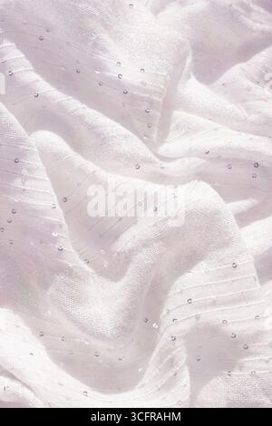 The soft white fabric, gently draped, reveals a textured surface decorated with small shimmering beads and sequins that perfectly capture the light in Stock Photo