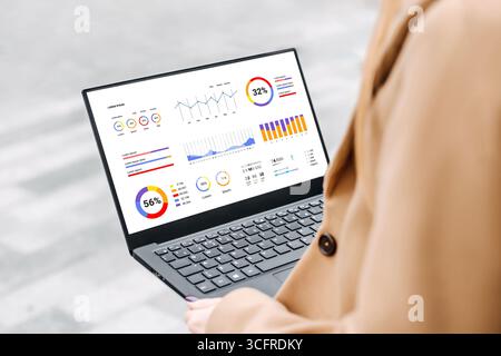 woman sitting outdoors with laptop and financial charts, a graph of analytics and statistics at screen Stock Photo