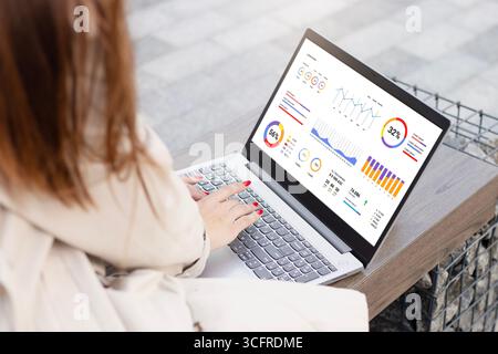 woman with laptop with financial charts at screen. female hands lie on a laptop keyboard with a graphs at white screen, typing text Stock Photo