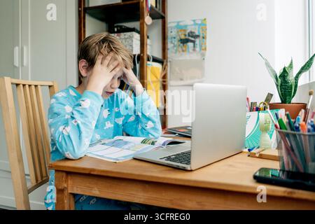 A tired, upset boy overloaded with information sits at his desk and does his homework. Stock Photo