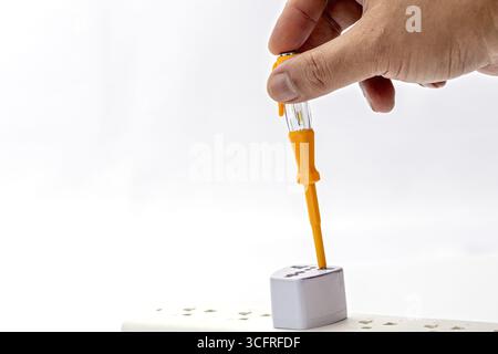 A hand using tester screwdriver on power strip socket, electrical safety check, white background, close up, indoor, precaution Stock Photo