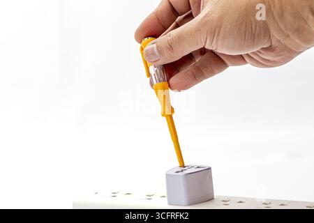 A hand using voltage tester on socket, electrical safety, testing power outlet, white background, caution, close up, indoor Stock Photo