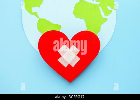 World health day concept. Paper model of earth globe red heart with cross isolated on blue background Stock Photo
