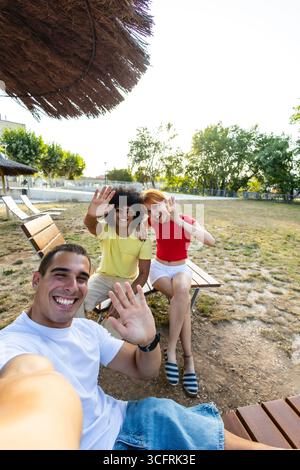 Happy friends taking selfie waving at camera in a park Stock Photo