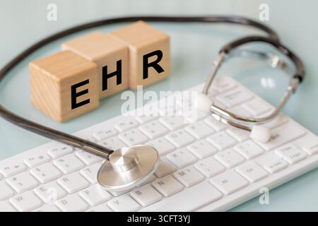 EHR, Electronic Health Record, written on wooden blocks. Doctor's office, Stethoscope and computer keyboard. A digital system for collecting and stori Stock Photo