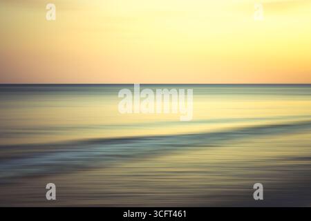 Warm tones of golden hour cast over the ocean and smooth rolling waves. Stock Photo