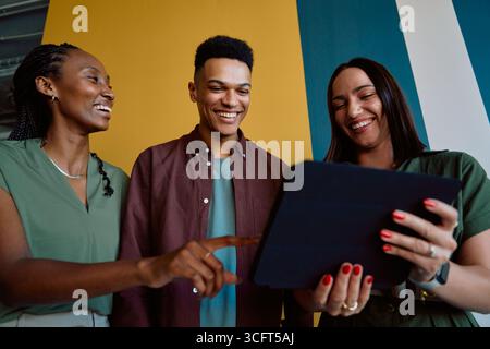 Happy young colleagues using digital tablet during casual meeting in office during daytime Stock Photo