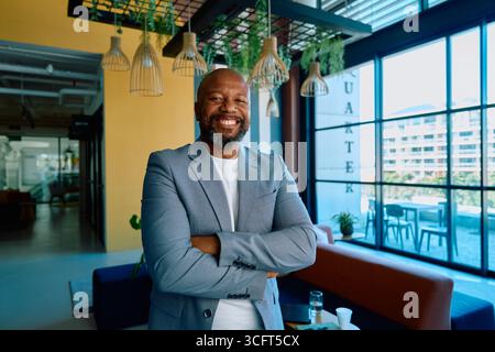 Portrait of cheerful mature businessman in blazer standing arms crossed in office during daytime Stock Photo