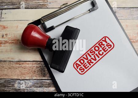 Red Handle Rubber Stamper and Advisory services text above clipboard isolated on wooden background Stock Photo