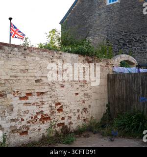 Rustic English Patriotism: A Glimpse of Everyday Life Behind a Weathered Wall with washing hanging to dry and a Union Flag Stock Photo